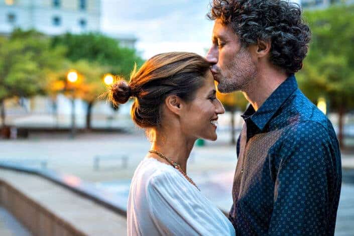 Romantic senior man giving a kiss to her woman in the city street