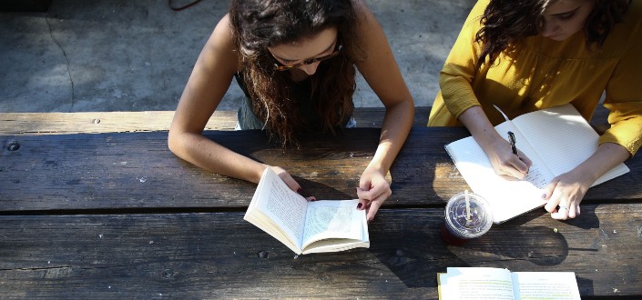 Two girls reading and writing on a bench