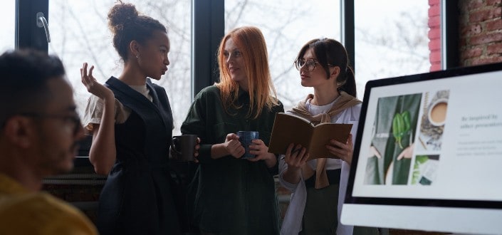 Three girls talking beside a window.