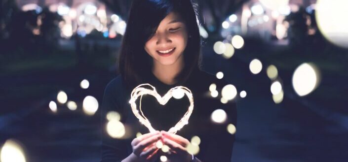 smiling woman holding a heart-shaped light at night