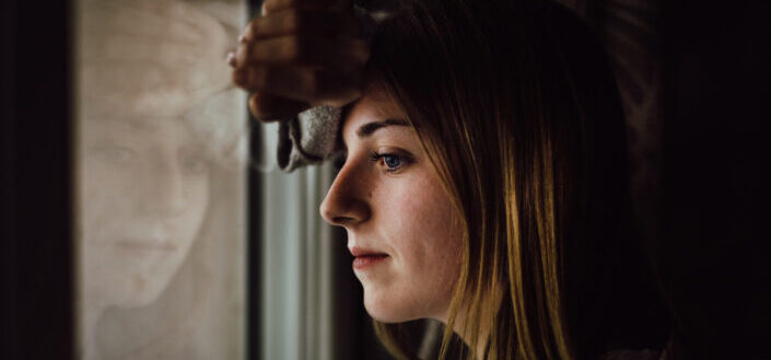 Serious woman looking outside through her window