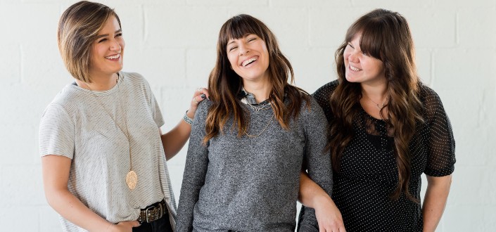 three women smiling with a white wall background
