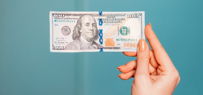 one hundred dollar bill held by a woman's hand