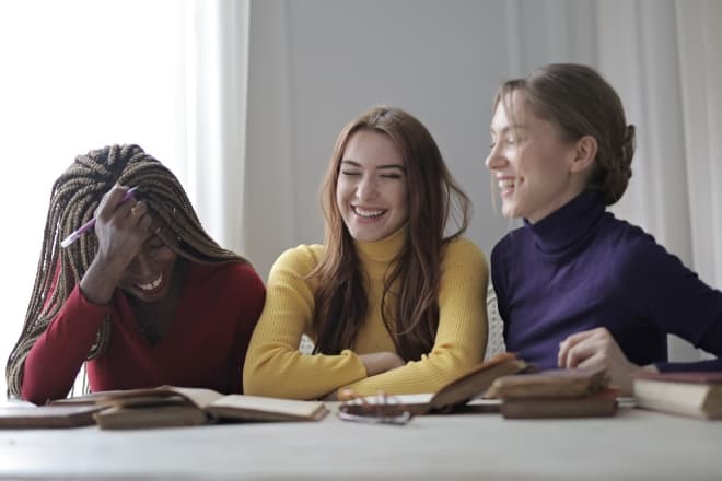 Three girl friends laughing together while studying - funny questions