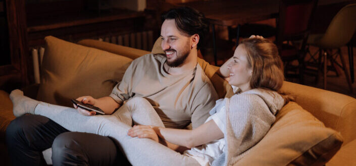 Couple, cuddling on a couch, happily watching TV.