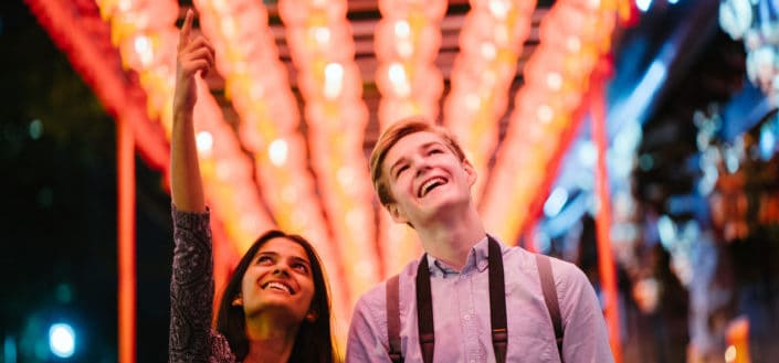 Couple, delighted under the festive lights.