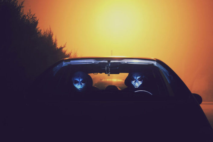 Two alien-faced creatures, riding a car.