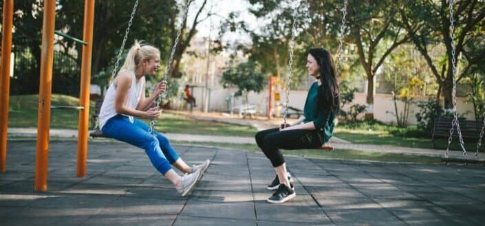 Two girls having fun talking while swinging.
