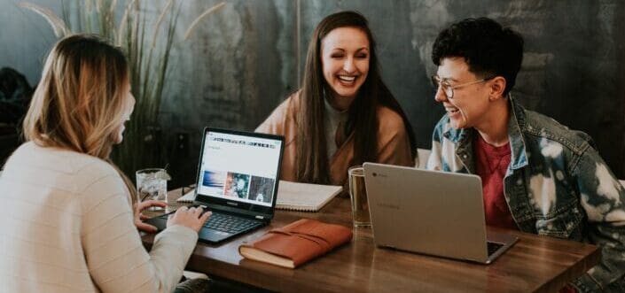 Three women happily chatting while working on their laptops.