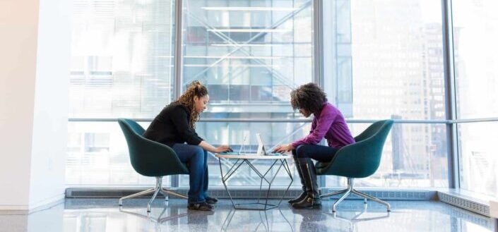 Two women chatting while working on their laptops.