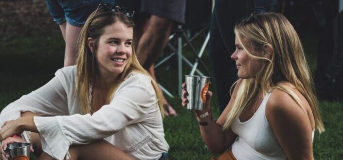 Two ladies on a party, talking while drinking.