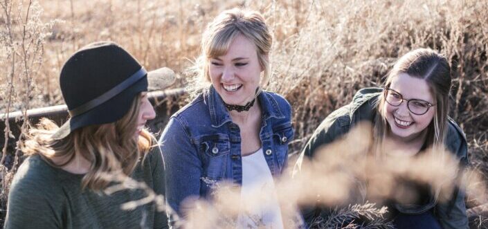 Three girls laughing together in the field.