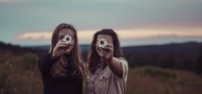 Two girls holding out a flower each.