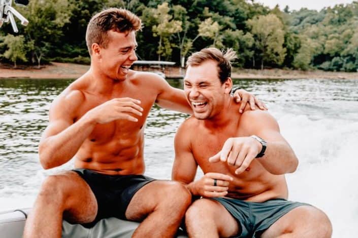Two topless guys laughing together by a river