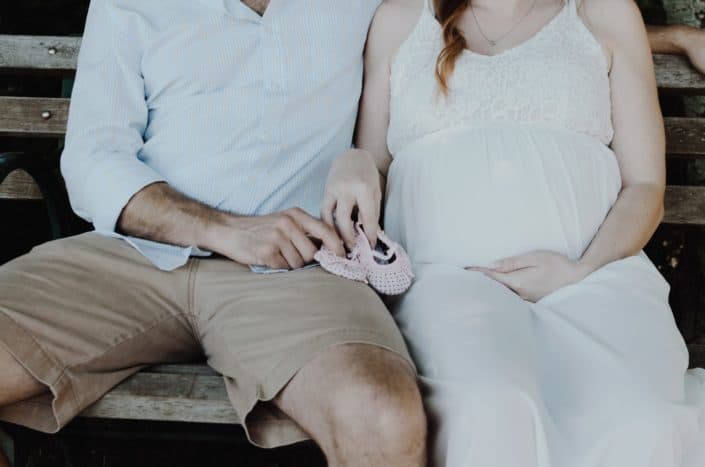 Father and pregnant mother holding baby shoes
