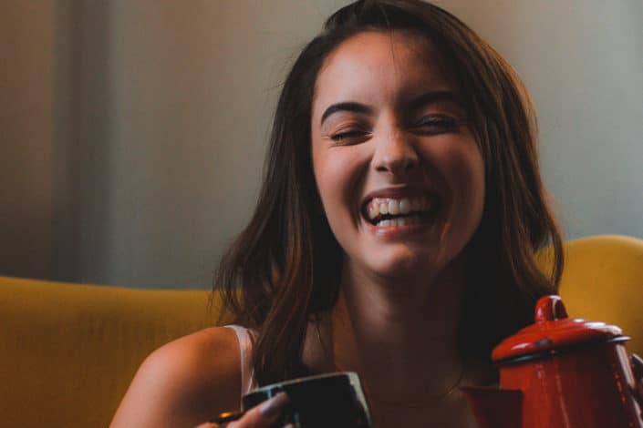 A woman laughing holding a mug and kettle