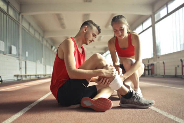 Girl helping guy teammate bandage his leg.