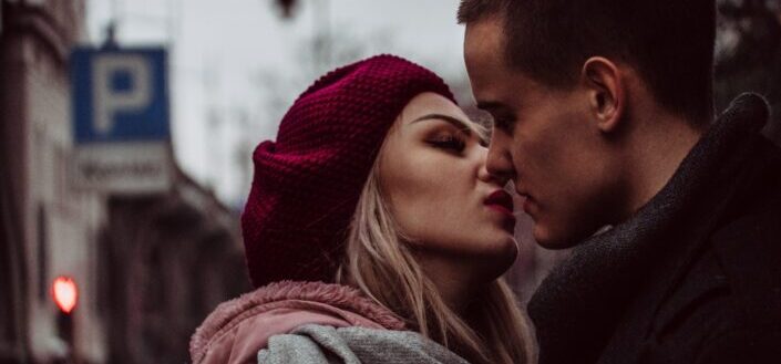 man and woman standing while kissing beside street signage