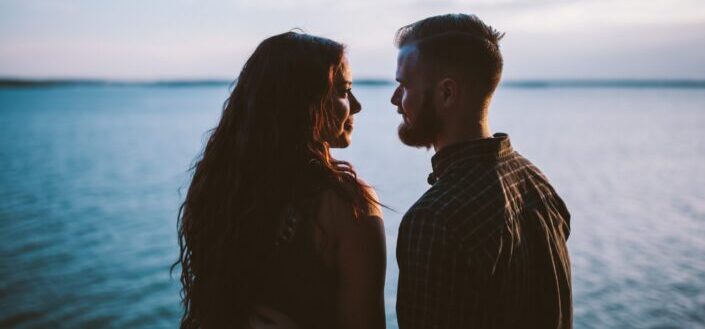 man and woman standing while looking each other near body of water
