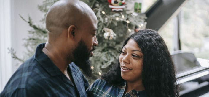 Positive black couple standing close near fir tree