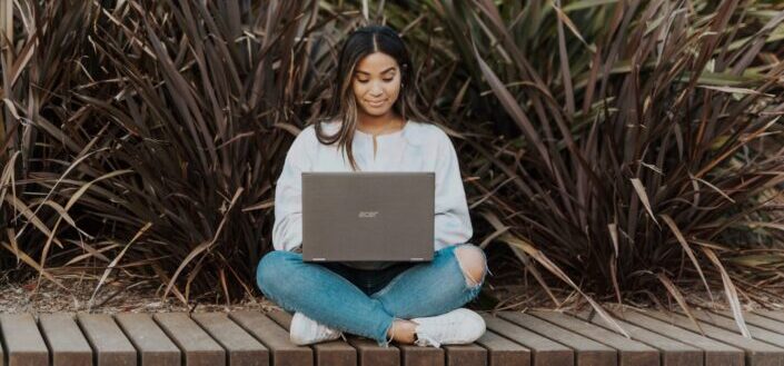 woman sitting on a wooden ledge using laptop