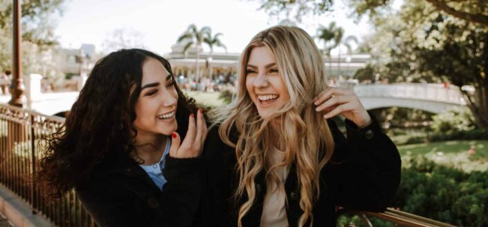 two women smiling and standing near trees