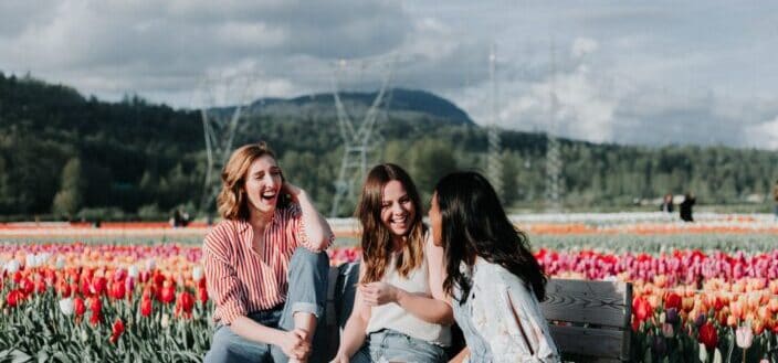 three women sitting on a bench near flowers