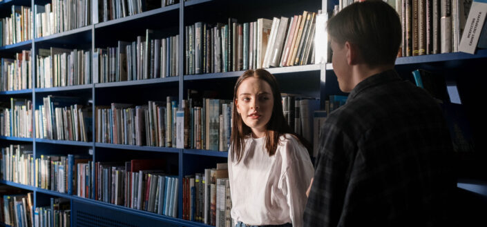 Two people standing near bookshelves