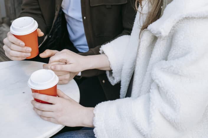 Cropped couple holding hands while holding coffee