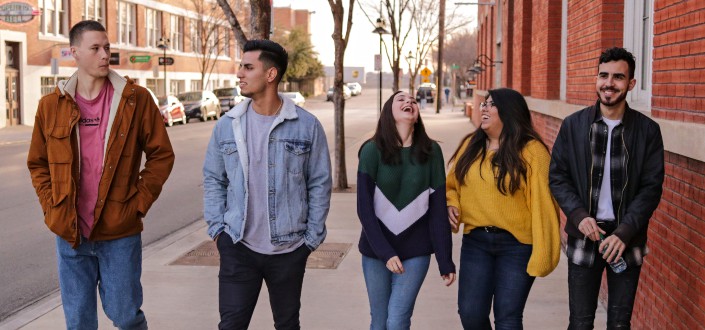 three men with two women laughing while walking side by side
