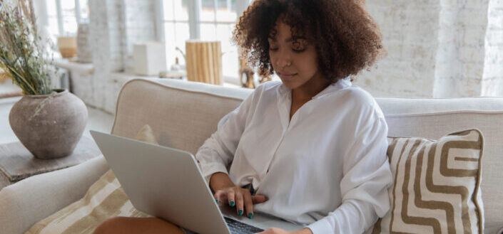 Young lady typing on laptop sitting on couch