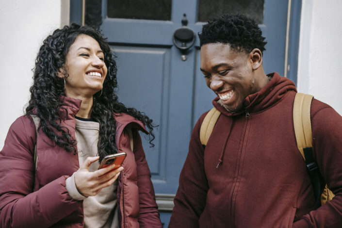 Friends with smartphones laughing near door of building