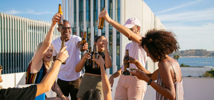 Joyful group of friends toasting with beer bottles on rooftop
