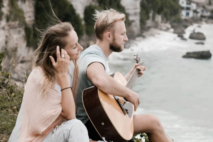 Peaceful young couple playing guitar on hill 
