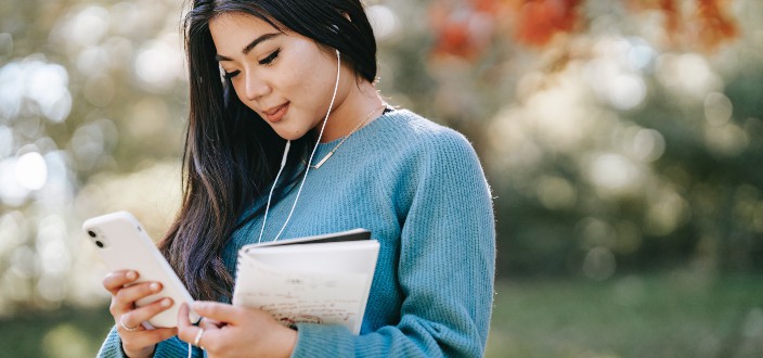 A woman wearing earphones smiling at her phone