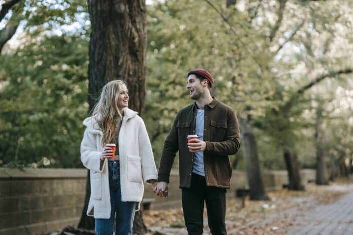 positive young couple holding hands and drinking coffee
