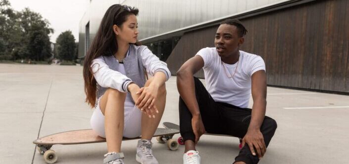 Skater couple talking while sitting on their skateboards.