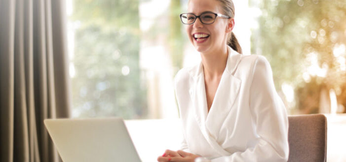 Laughing businesswoman working in office with laptop