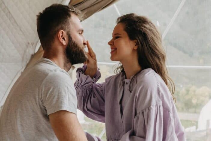 Wife touching husband's nose while sitting on bed