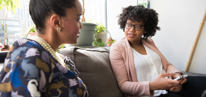 Two well-dressed women sitting on a couch while talking.