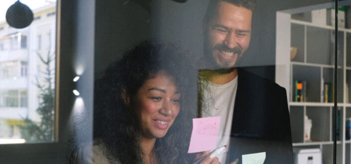 Multiethnic cheerful colleagues looking at stickers and smiling