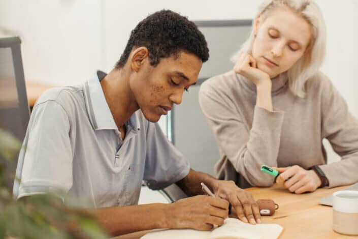 Woman Sitting Beside Man Writing on Notepad