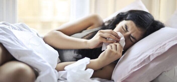 Woman Lying on Bed While Blowing Her Nose