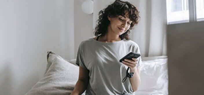 Woman sitting on a bed while texting.