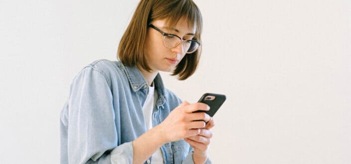 Lady wearing a faded denim jacket and eyeglass looking at her phone