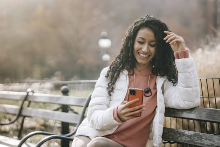Woman smiling at here phone while sitting at a bench