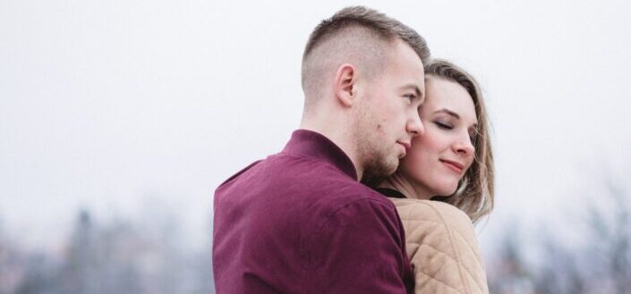 man hugging woman while standing on snowy weather