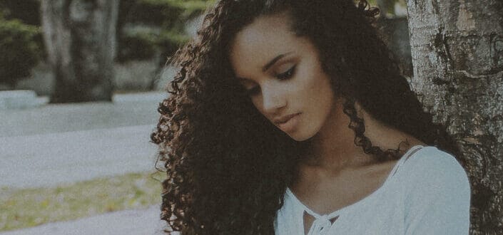 Curly haired woman sitting under the tree while having some deep thoughts