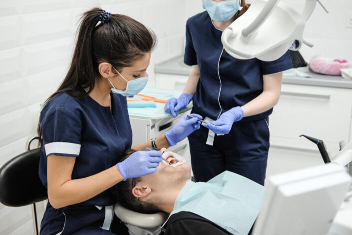 Female dentist with assistant curing teeth of patient