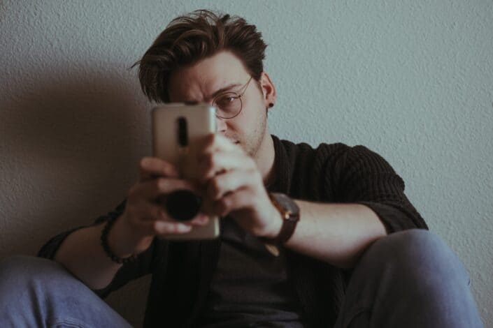 Man leaning on a wall reading a message on his phone.